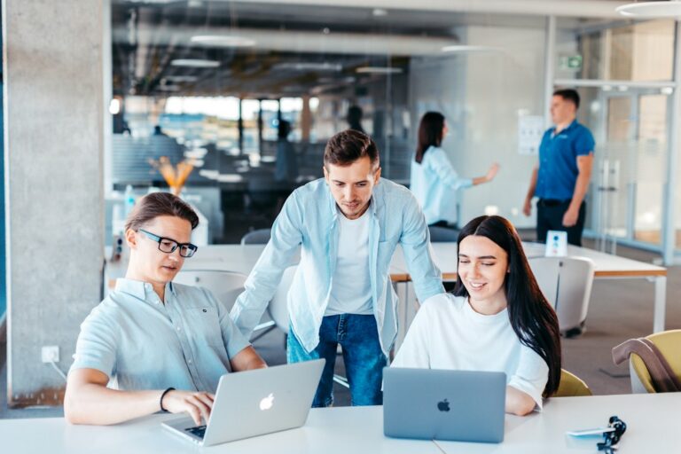 Trois collègues travaillent ensemble autour d’une table avec leurs ordinateurs