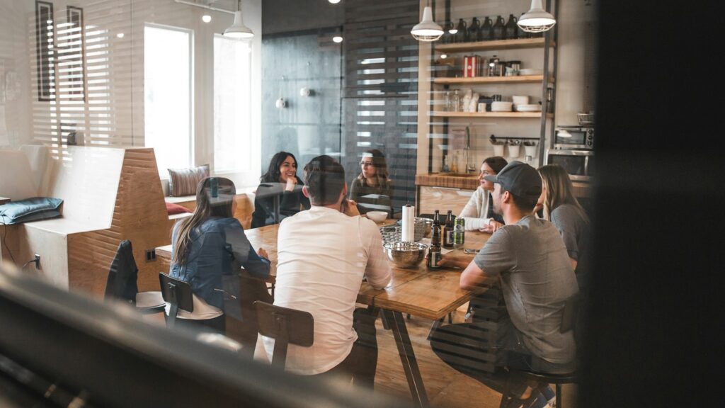Des collègues échangent autour d’une table de réunion avec leurs ordinateurs.